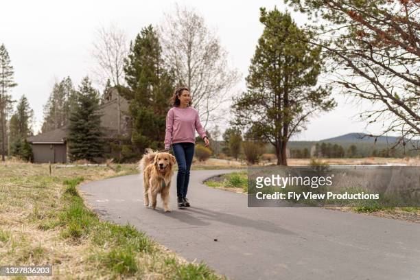 woman walking with her pet dog on paved walking trail - pet leash stockfoto's en -beelden