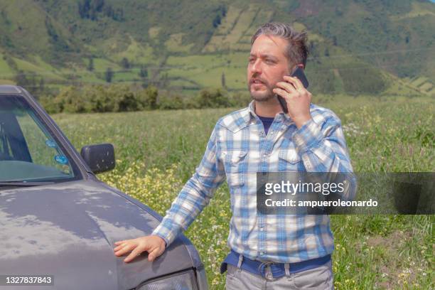 junger männlicher manager landwirt mit einer 5g-technologie, die per handy spricht. auf der rückseite ein grünes chochos-feld an einem sonnigen tag im ecuadorianischen hochland. er trägt ein weißblaues hemd und eine graue jeanshose. - autobauer stock-fotos und bilder
