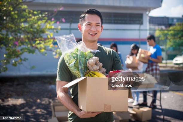 cheerful and smiling asian male volunteer and his colleagues distributing grocery food at community food bank - food pantry stockfoto's en -beelden