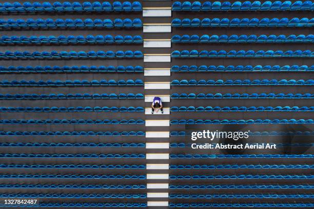 aerial image looking down on one person sitting amongst empty stadium seating, united kingdom - arranging ideas stock-fotos und bilder