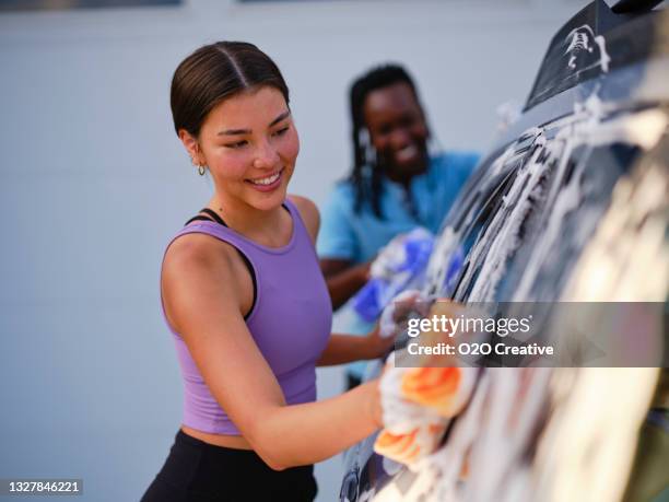 young couple washing a car in a driveway - young woman getting wet at car wash smiling stock pictures, royalty-free photos & images