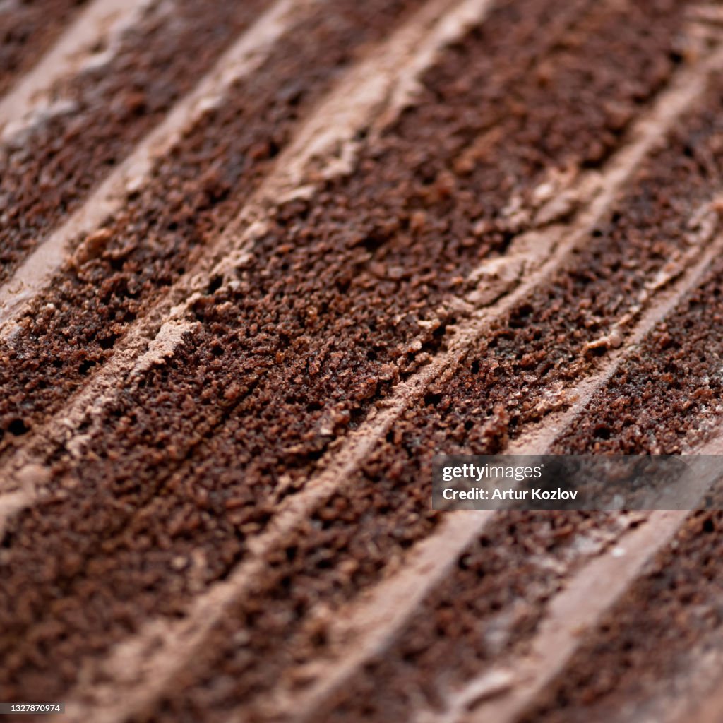 Chocolate cake texture or background. Piece of brown layered dessert with cream. Close-up shot. Soft focus
