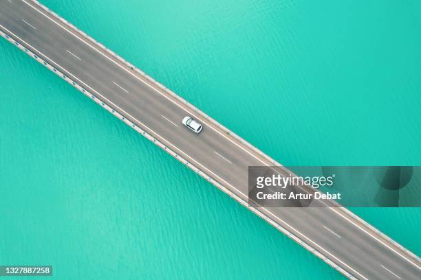 drone view following car from above driving on bridge crossing blue lake in the pyrenees mountains. - auto mieten stock-fotos und bilder