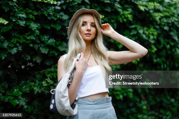 German Model Anna Hiltrop wearing a white cropped top by Jan "u2019n June, pastel blue-grey pants by Heaven Lab, a cream colored bucket hat by...