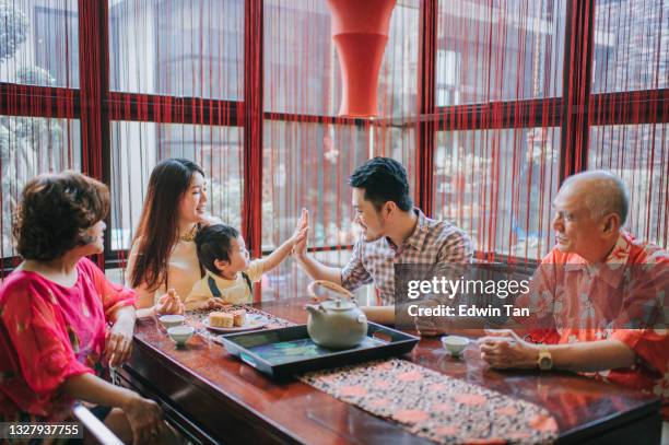 アフタヌーンティーの集まり中に自宅で伝統的な中秋のムーンケーキと中国茶を楽しんでいる間、息子と一緒に中国の父親ハイ5 - 中秋節 ストックフォトと画像