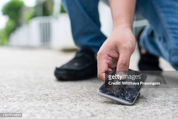 man picking up broken smartphone from the ground - broken cell phone stock-fotos und bilder