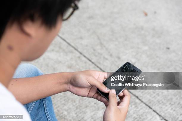 displeased man holding smartphone with broken screen - broken smartphone fotografías e imágenes de stock