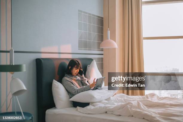アジアの中国の十代の少女は、携帯電話に話し、友人と日没時にベッドの上にデジタルタブレットを使用しています - asian girl doing online shopping ストックフォトと画像