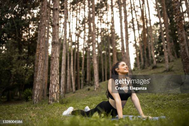 young athletic woman in cobra pose practicing yoga in forest. young woman practicing yoga, doing upward facing dog exercise, urdhva mukha shvanasana pose, working out, wearing sportswear, black pants and top - forest cobra stock pictures, royalty-free photos & images