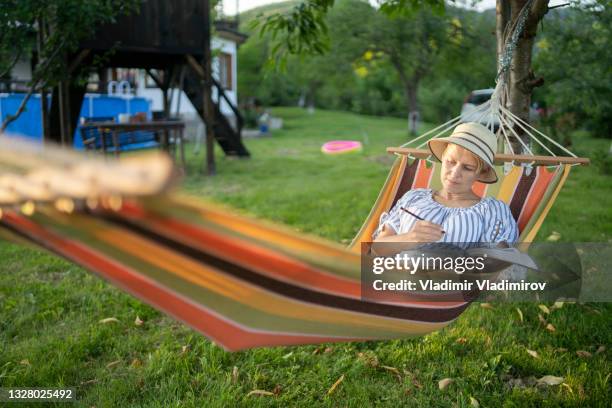 a woman with sun hat drawing while resting in her garden - backyard hammock stock pictures, royalty-free photos & images