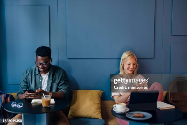 zwei junge universitätsstudenten mit mobiltelefonen in einem café - ohrhörer stock-fotos und bilder