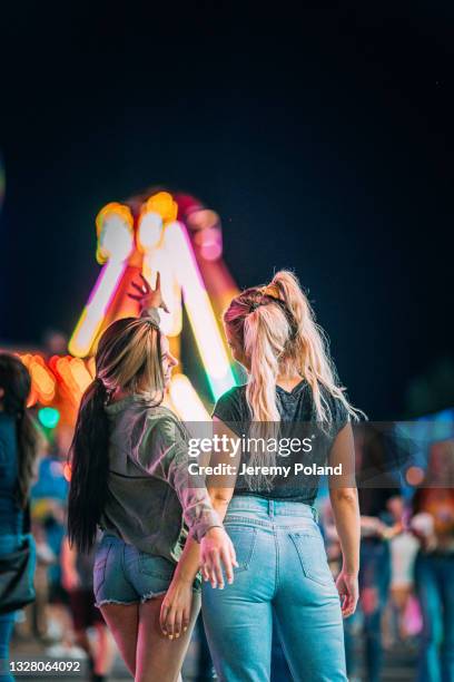 two beautiful young women best friends facing away from camera and laughing together at a late night traveling carnival in the summer - fiesta posterior 個照片及圖片檔