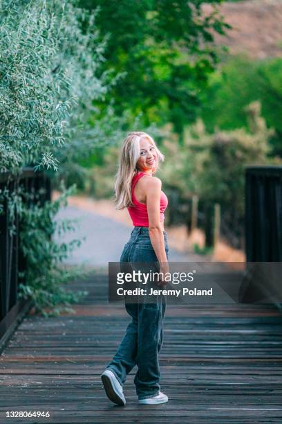 artistic portrait of a young woman looking over her shoulder as she walks across a bridge alone at dusk - baggy jeans stockfoto's en -beelden