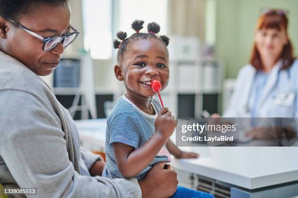 colpo di un'adorabile bambina che si fa un lecca-lecca dal suo medico durante un controllo con sua madre - doctor with child foto e immagini stock