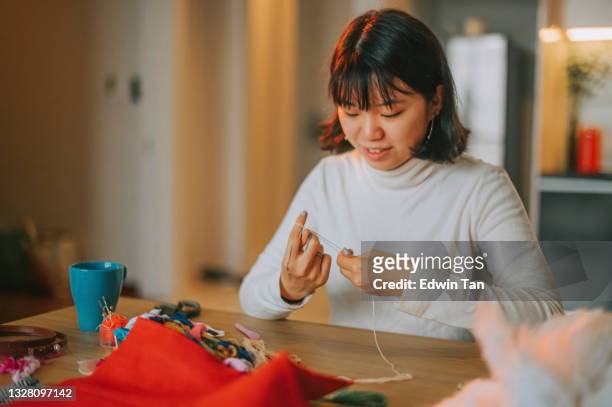 asian chinese teenage girl tying thread preparing for cross-stitch embroidery handcraft during evening at home side hustle - embroidery stock pictures, royalty-free photos & images