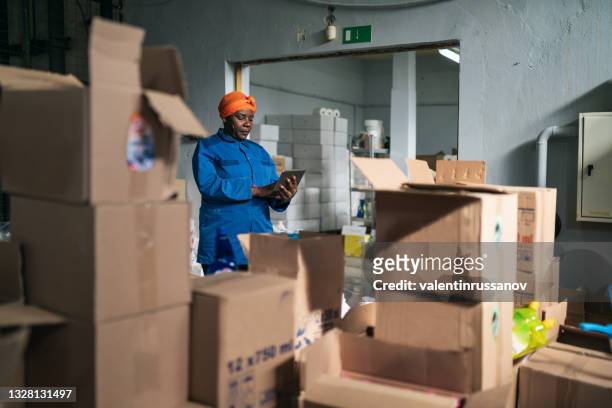 afro female warehouse worker checking the shipment delivery on a digital tablet in distribution warehouse - country market stockfoto's en -beelden