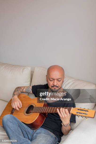 man sitting on his sofa practicing the chords on his guitar while at home alone - acoustic music stock pictures, royalty-free photos & images