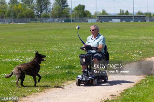 hombre discapacitado lanzando pelota para que su perro lo busque mientras conduce un scooter de movilidad, demostrando que la discapacidad no le impide disfrutar de las cosas simples de la vida como el ejercicio de nuestras queridas mascotas. - mobility scooter fotografías e imágenes de stock
