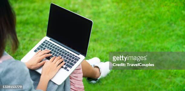 woman sitting on grass at park working on laptop. young woman's legs on the green grass with open laptop. girl's hands on keyboard. distance learning concept - girl sitting with legs open stock pictures, royalty-free photos & images