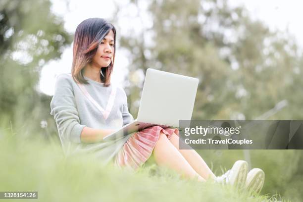 woman sitting on grass at park working on laptop. young woman's legs on the green grass with open laptop. girl's hands on keyboard. distance learning concept - girl sitting with legs open stock pictures, royalty-free photos & images