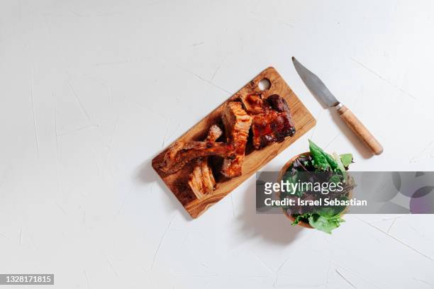 view from above of delicious charcoal grilled ribs cut on an olive wood board accompanied by a salad of various lettuces. - pork cuts stock pictures, royalty-free photos & images