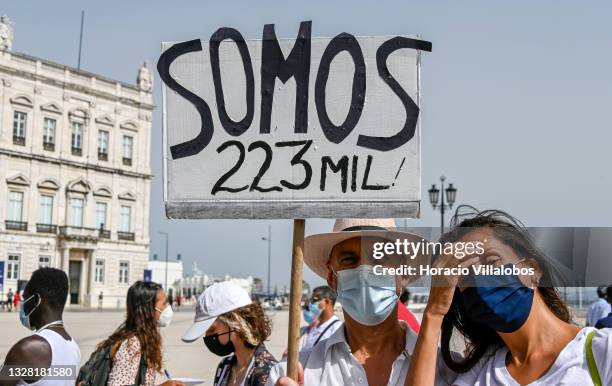 Mask-clad couple hoist a placard with the number of immigrants who were included in a government's decree of temporary regularization but still wait...