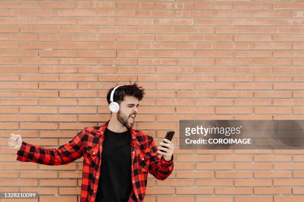excited young man using his phone against a brick wall - brick phone stock pictures, royalty-free photos & images