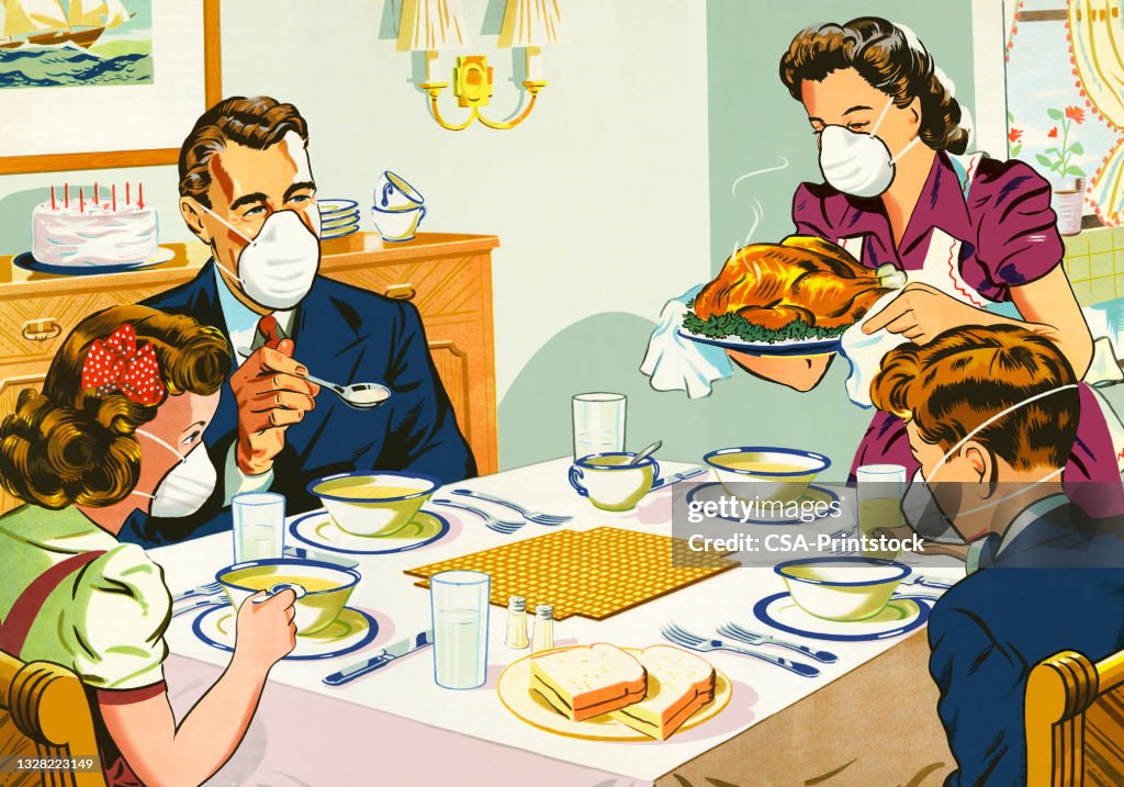 Familia con máscaras faciales en la mesa de la cena