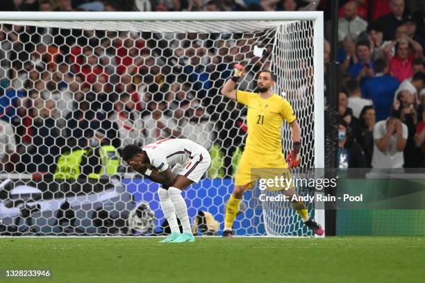 Marcus Rashford of England looks dejected after hitting the post in their team's third penalty as Gianluigi Donnarumma of Italy celebrates in a...