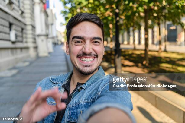携帯電話を持つ散歩中の若い男は、シティストリートの仕事に向かい、自分撮りをしています。 - セルフィー　男性 ストックフォトと画像