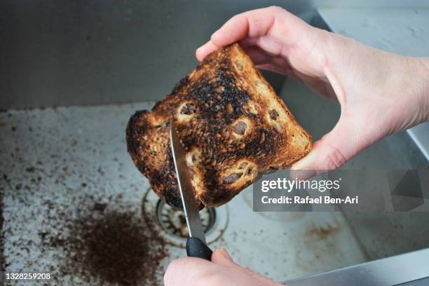 person holding and removing burnt from a toast with a kitchen knife - burnt cooking stock pictures, royalty-free photos & images