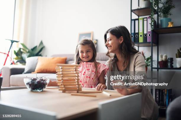 young mother and little daughter playing jenga in living room - block removal game stock pictures, royalty-free photos & images