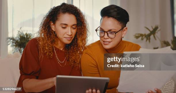 shot of a young lesbian couple doing paperwork while using a digital tablet at home - lesbian couple stock pictures, royalty-free photos & images