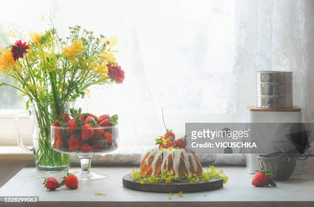 still life with bundt cake on kitchen table with strawberries, flowers and kitchen utensils at window background - cake decoration stock pictures, royalty-free photos & images