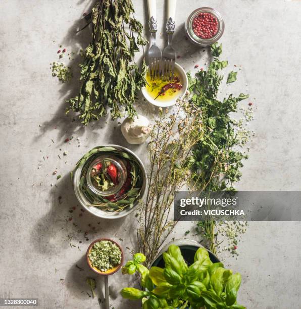 various kitchen flavor herbs on pale concrete kitchen table with bowls, forks and spices - herbs stockfoto's en -beelden