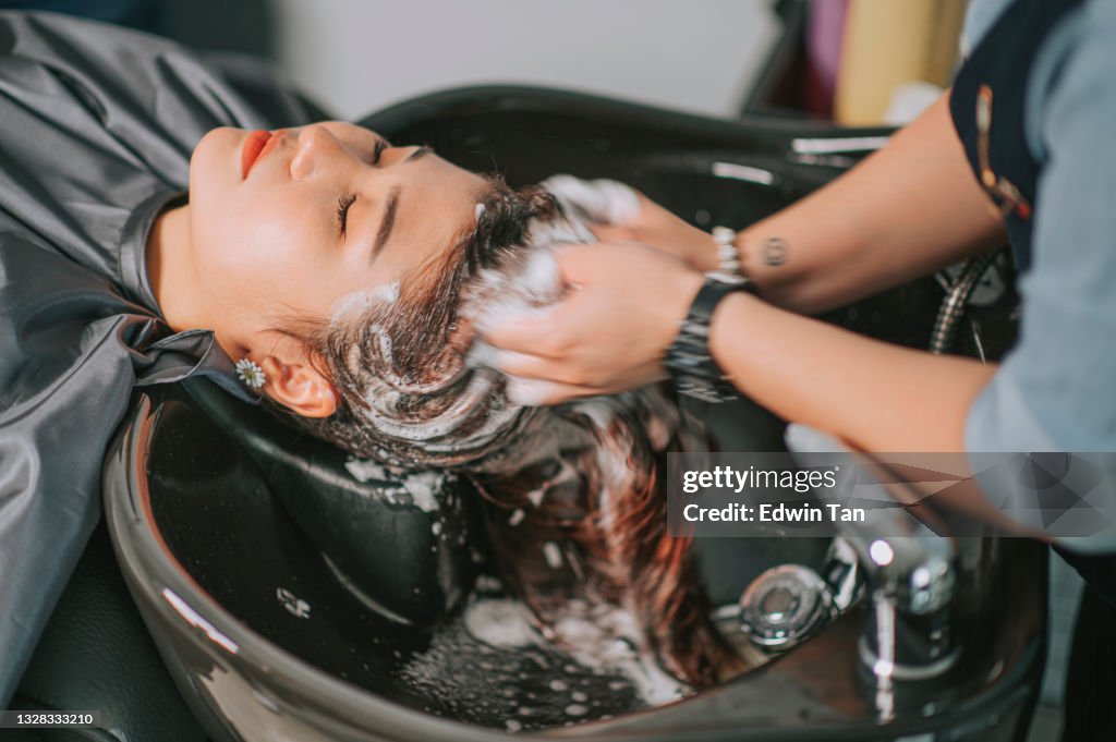 Direkt über asiatischer Chinesischer Frau, die sich mit geschlossenen Augen zur Haarwäsche im Friseursalon hinliegt