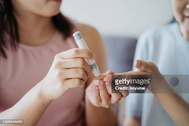 close-up woman helping her mother check blood sugar level using a blood glucose meter at home - diabetic stockfoto's en -beelden