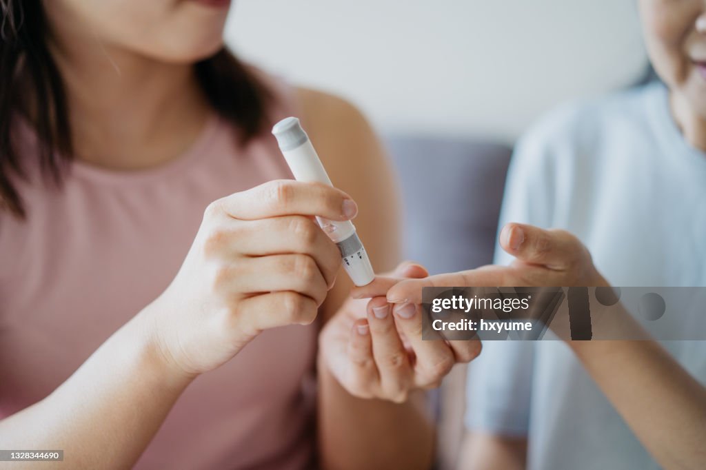 Close-up mulher ajudando sua mãe a verificar o nível de açúcar no sangue usando um medidor de glicose no sangue em casa