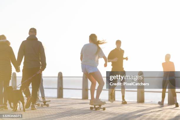 skateboarder riding between people on boardwalk - longboard skating stock pictures, royalty-free photos & images