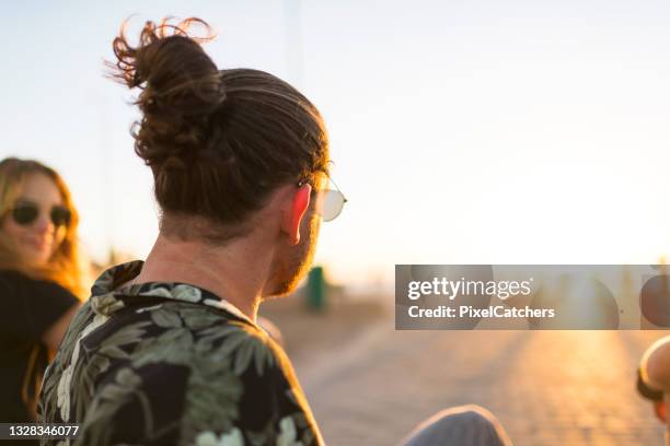 back view young man with long hair tied up in bun looking to sunset - summer hair bun stock pictures, royalty-free photos & images