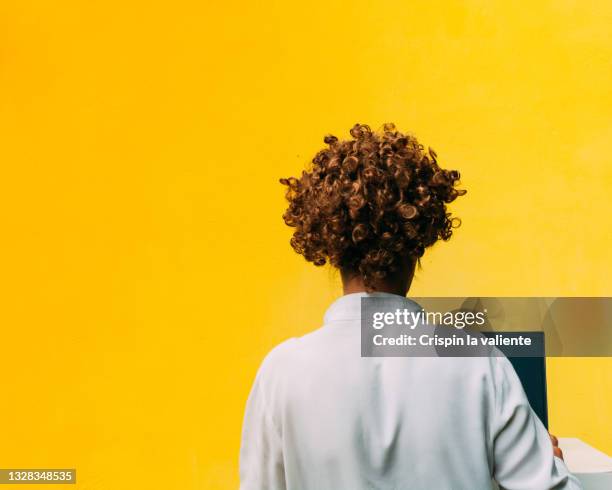 back view of woman with short curly hair using computer, yellow background - nicht erkennbare person frau stock-fotos und bilder