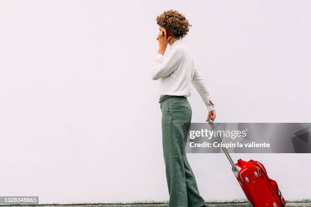woman with short curly hair talking on the phone and dragging her red suitcase on white background - pulling fotografías e imágenes de stock