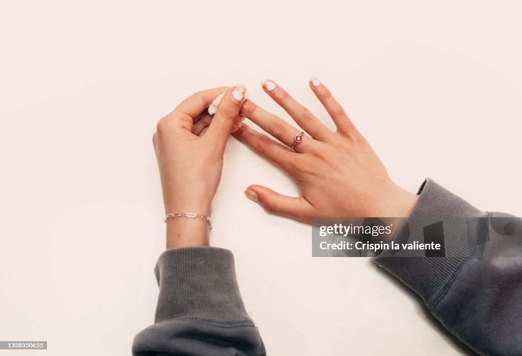 Hands Of young Woman Removing Nail Polish Against White Background