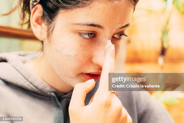 close-up of teenage girl pouring cream on her face, skin care - huidaandoening stockfoto's en -beelden