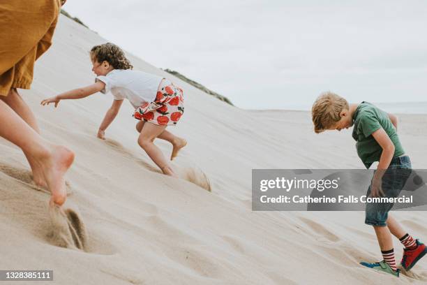 three children clamber up a steep sand dune, which takes a lot of effort as the soft sand gives way under their little feet and hands - batalha da grã bretanha imagens e fotografias de stock