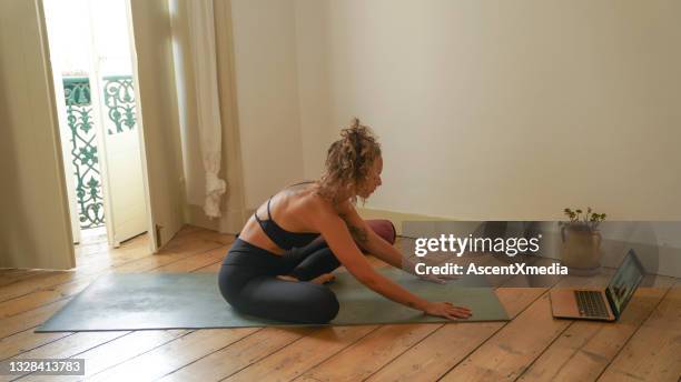 young woman follows online yoga class on laptop at home - body bending forward stock pictures, royalty-free photos & images