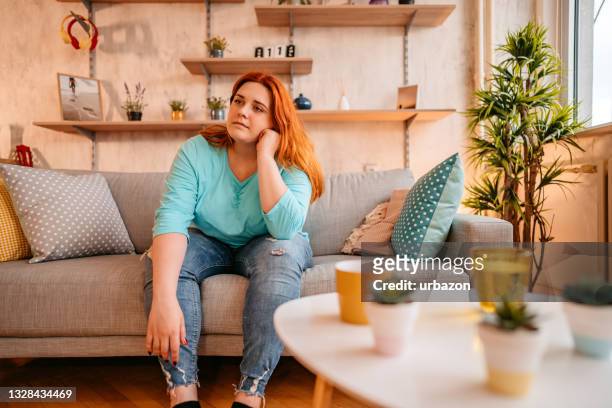 frau, die allein zu hause sitzt und traurig und verzweifelt aussieht - stressed young woman sitting on couch stock-fotos und bilder