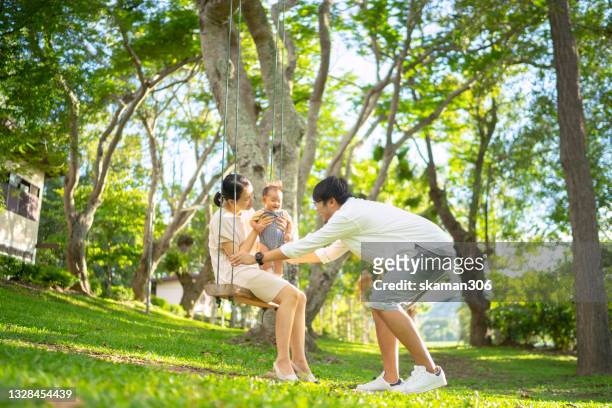 candid beautiful moment asian family with one child wearing casual cloth leisure outdoor activity  and playing swing under the tree with warming light and tone domestic life concept - domestic life imagens e fotografias de stock