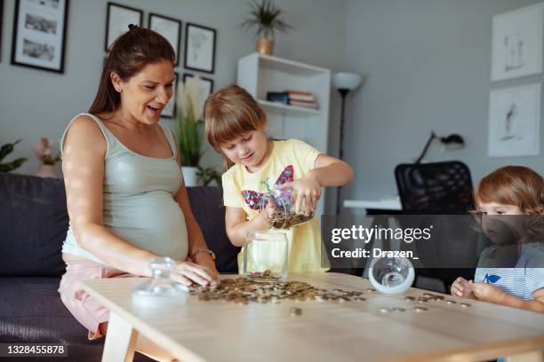pregnant mother with daughters at home, collecting coins in jar - jar stock pictures, royalty-free photos & images
