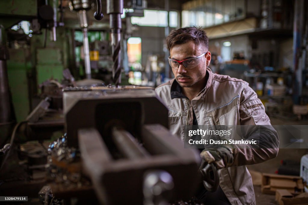 Focused milling machine operator, controlling the machine work at the metal workshop